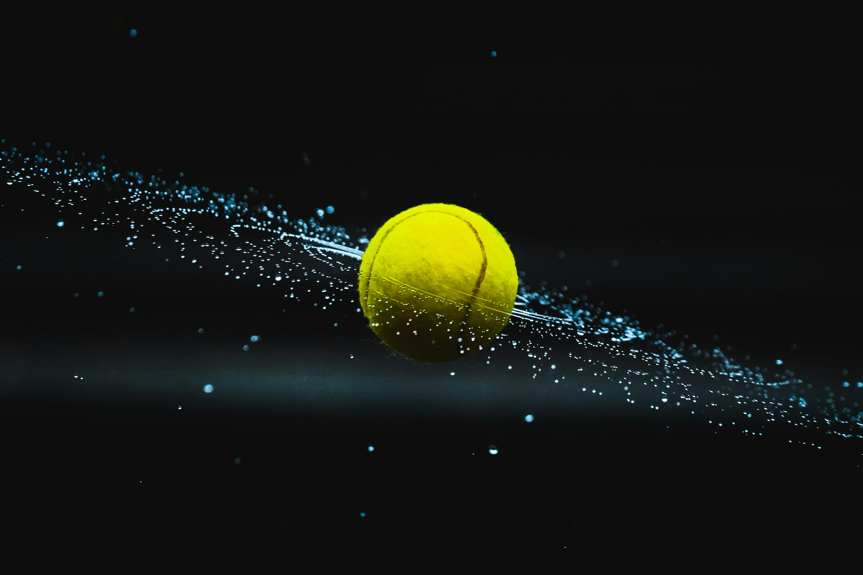Tennis ball spinning in the air with water droplets flying off